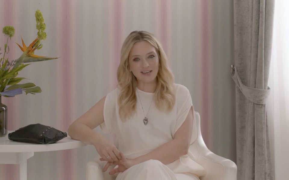 Blonde host seated against a pink-striped backdrop for ELLE's My Beauty Bag branded content