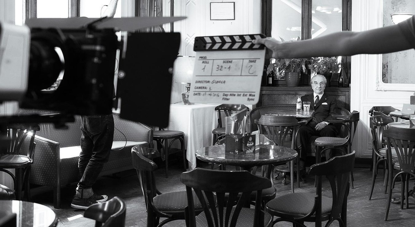 Set del docufilm su Gualtiero Marchesi: il maestro seduto al tavolino, in primo piano la macchina da presa e il ciak firmato Gigola